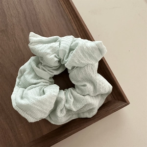 Detailed texture of a mint green pleated fabric scrunchie on a wooden tray