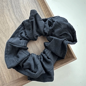 Close-up of black fabric scrunchie with fine texture on a wooden minimalist tray