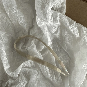 Close-up of elegant U-shaped acetate hair pin with cream marble texture on white paper