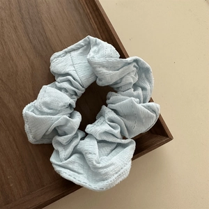 Detail shot of light blue fabric hair scrunchie with soft folds on a wooden tray