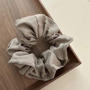 Detailed texture of beige pleated fabric scrunchies on a minimalist wooden tray