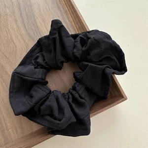 Macro detail of black waffle texture fabric scrunchie on a minimalist wooden tray