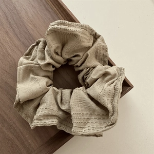 Detailed close-up of khaki scrunchie with dashed embroidery on cotton-linen fabric