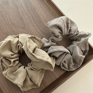 Detailed macro of beige and taupe fabric scrunchies on a wooden tray with linen texture