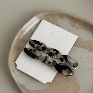 Close-up of twisted marble acetate hair clips with golden metal base on a ceramic tray