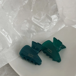 Detailed close-up of dark green translucent acetate hair claws with gold Amy Bear logo