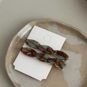 Detail of twisted acetate hair clips with retro marble patterns on a ceramic tray