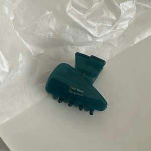 Detail shot of a dark green acetate claw clip with gold Amy Bear logo engraving