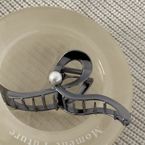 Detail of wave-shaped gunmetal hair claw clip with a white pearl on a warm fabric background