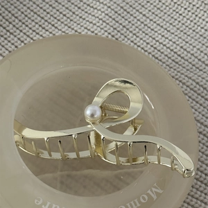 Detailed view of wave-shaped golden metal hair claw clip with a single white pearl accent