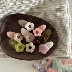 Barrettes à fleurs en résine aux tons Morandi disposées sur un plateau en bois