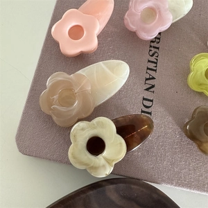 Détail de pinces à cheveux fleur en acétate coloré sur un fond en tissu texturé
