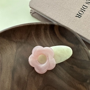 Détail de la pince à cheveux fleur en résine rose avec texture marbrée sur bois