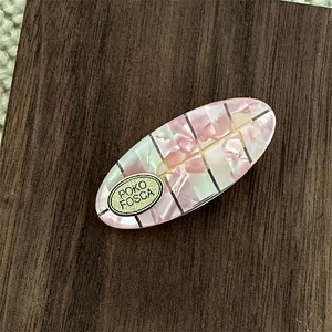 Oval acetate hair clip with pink mermaid shell texture and gold plaque on wood