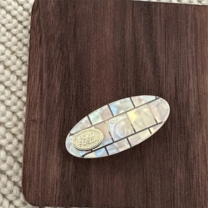 Macro shot of oval checkered hair clip with mother-of-pearl texture and golden metal piece
