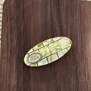 Close-up of oval acetic acid hair clip with mosaic texture and metal logo plaque
