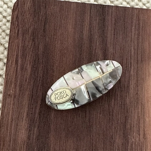 Detail showing an oval mermaid mosaic hair clip with a gold POKO FOSCA metal logo