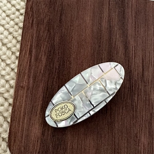 Macro detail of oval acetate hair clip with grey marble texture and gold plaque