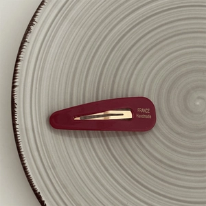 Macro detail of dark red acetate hair clip with gold lettering on a ceramic tray