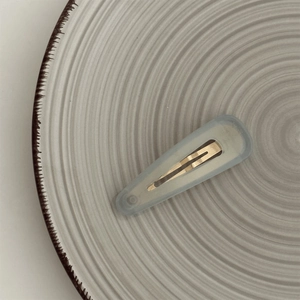 Detail of light blue-gray translucent teardrop BB clip on white ceramic plate
