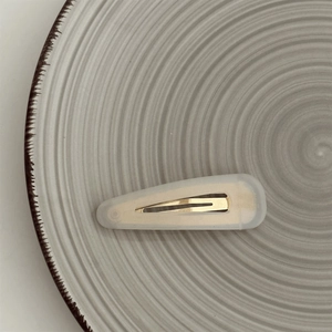 Close-up of a cream triangle hair clip on a textured ceramic plate in soft natural light