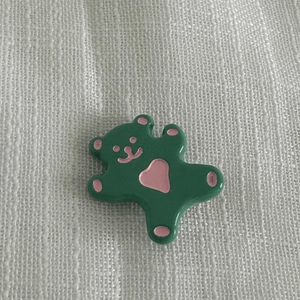 Détail d'une pince à cheveux ours vert brillant avec cœur rose sur tissu blanc