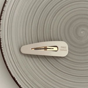 Detail of cream-colored handmade BB hair clip with gold metal base on a ceramic plate