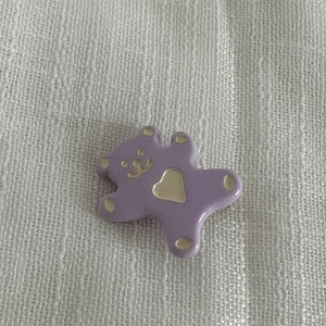 Gros plan détaillé d'une breloque ours violette avec cœur doré sur tissu blanc