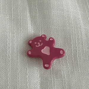Détail de la broche ours rose vif avec motif de cœur sur un fond de tissu blanc