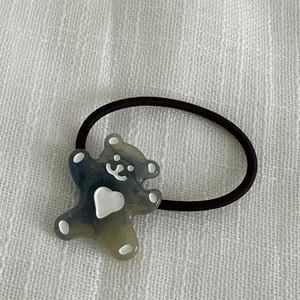 Détail d'un élastique à cheveux ours en résine grise avec motif cœur sur tissu blanc