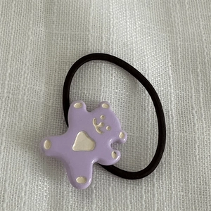 Détail d'un chouchou ourson violet en résine avec cœur sur tissu texturé blanc