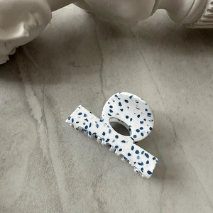 Detail of blue terrazzo acetate hair claw clip on marble background with white statue