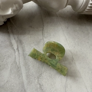 Detail of green and yellow marble pattern acetate hair claw clip with stone background