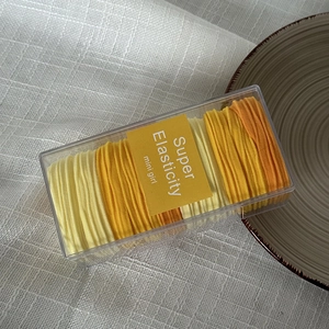 Detail view of high elasticity hair ties set in clear box with yellow tones