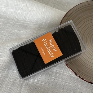 Detail of boxed black high elasticity hair ties in transparent storage box with label
