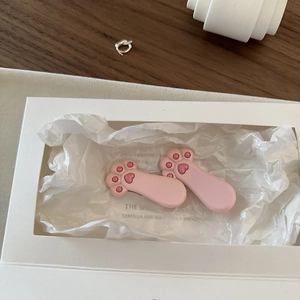 Dettaglio di fermagli per capelli a zampa di gatto rosa con cuori su sfondo di carta bianca