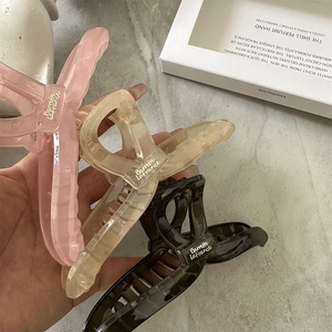 Three oversized resin hair claws in pink, amber, and brown with gold logo accents