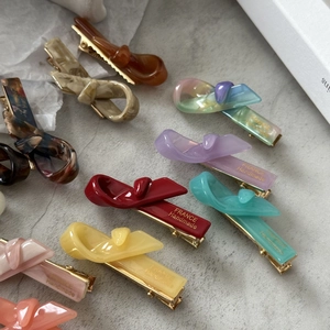 Barrettes à cheveux nœud en résine colorée avec logo doré sur fond gris texturé