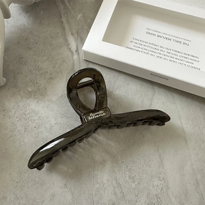 Macro detail of dark brown translucent hair claw clip with white logo on marble stone
