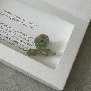 Détail d'une mini pince à cheveux en acétate avec marbrures vert-rose et ressort doré