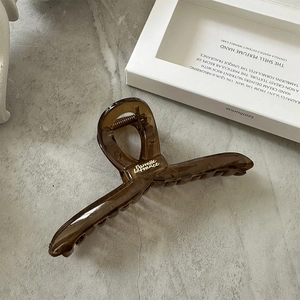 Detail of dark brown acrylic hair claw clip with gold spring and white text on stone