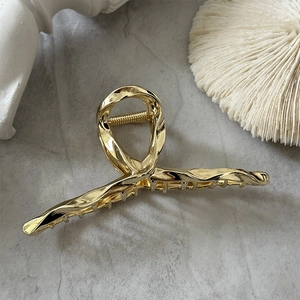 Détail d'une grande pince à cheveux en métal doré au design en spirale sur du marbre