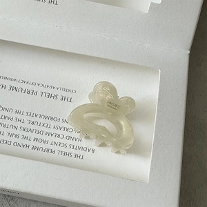 Detail of a pearlescent white acetate mini hair claw clip featuring an elegant logo design