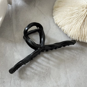 Gros plan détaillé d'une grande pince à cheveux noir mat sur un fond en marbre