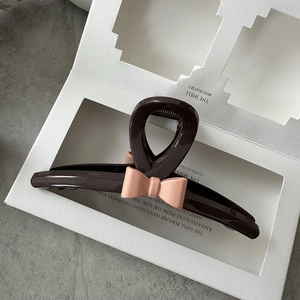 Detail shot of a dark brown resin hair claw clip with a pink bow on a white display stand