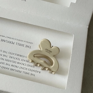 Detail shot of a cream-colored acetate hair claw with a gold label on a minimalist tray