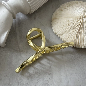 Détail d'une grande pince à cheveux en métal doré mat avec un design élégant de lignes croisées