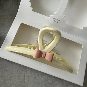 Detail of a cream resin hair claw clip with a pink bow in a premium gift box
