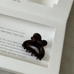 Close-up of handmade dark brown acetate hair claw with minimalist glossy finish on a stand