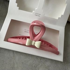 Detail of a large pink resin hair claw clip with a cream-colored decorative bow